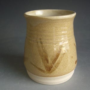 May include: A ceramic mug with a light brown glaze and brown leaf-like designs. The mug has a white rim and base.
