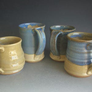 May include: Four handmade ceramic mugs in shades of blue and tan. Each mug has a unique glaze and a sturdy handle. The mugs are of varying heights and shapes, perfect for coffee or tea.
