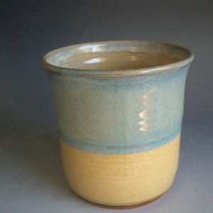 May include: A ceramic utensil holder with a light blue glaze on the top half and a yellow glaze on the bottom half.