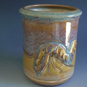 May include: A brown ceramic vase with a blue glaze and a raised leaf design.