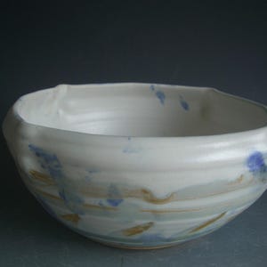 May include: A white ceramic bowl with blue and brown glaze. The bowl has a rounded shape and a slightly flared rim.