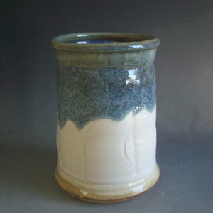 May include: A white ceramic mug with a blue and green glaze. The mug has a wavy rim and a textured design.