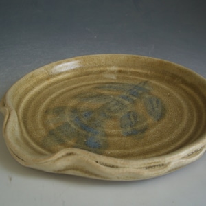 May include: A ceramic plate with a wavy edge and a brown glaze with blue accents. The plate has a slightly raised center.