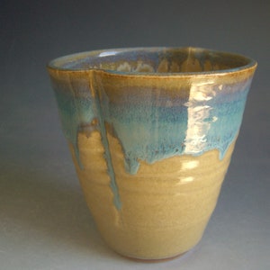 May include: A ceramic cup with a light brown glaze and a blue and green glaze on the top rim.
