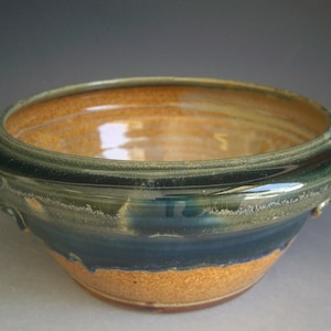 May include: A ceramic bowl with a dark blue glaze and a light brown rim. The bowl has two small handles on either side.