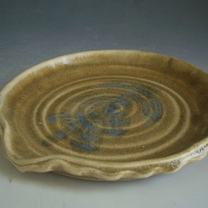 May include: A ceramic dish with a brown glaze and a blue swirl design. The dish has a wavy edge and is perfect for serving snacks or appetizers.