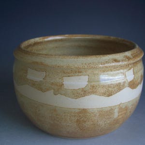 May include: A round, beige ceramic bowl with a white glaze. The bowl has a speckled texture and a white band around the top with a wavy edge.