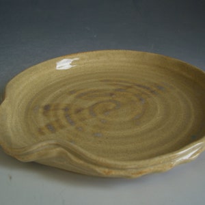 May include: A light brown ceramic dish with a wavy edge and a swirl pattern. The dish is glazed and has a slight sheen.