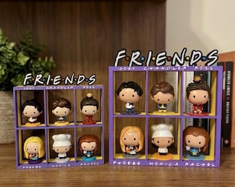 Può includere: Due scaffali viola e gialli con il testo "FRIENDS" in alto, ciascuno con sei statuette di personaggi. Le statuette sono dei personaggi della serie TV "Friends". Gli scaffali sono su una superficie di legno.