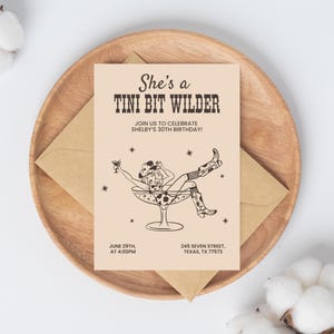Könnte beinhalten: Eine beigefarbene Einladungskarte mit einer Schwarzweißillustration einer Frau in einem Cowboyhut, die in einem Martini-Glas sitzt. Der Text auf der Karte lautet "She's a Tini Bit Wilder" und "Join us to celebrate Shelby's 30th Birthday!" mit dem Datum und der Uhrzeit der Veranstaltung, dem 29. Juni um 16:00 Uhr, und der Adresse, 245 Seven Street, Texas, TX 77573.