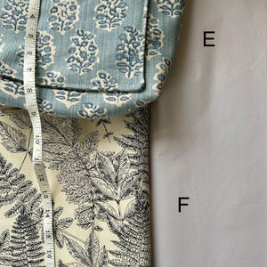May include: A light blue tote bag with a floral pattern and a cream-colored fabric with a black fern design. The bag is approximately 8 inches wide. The cream fabric is approximately 10 inches wide.