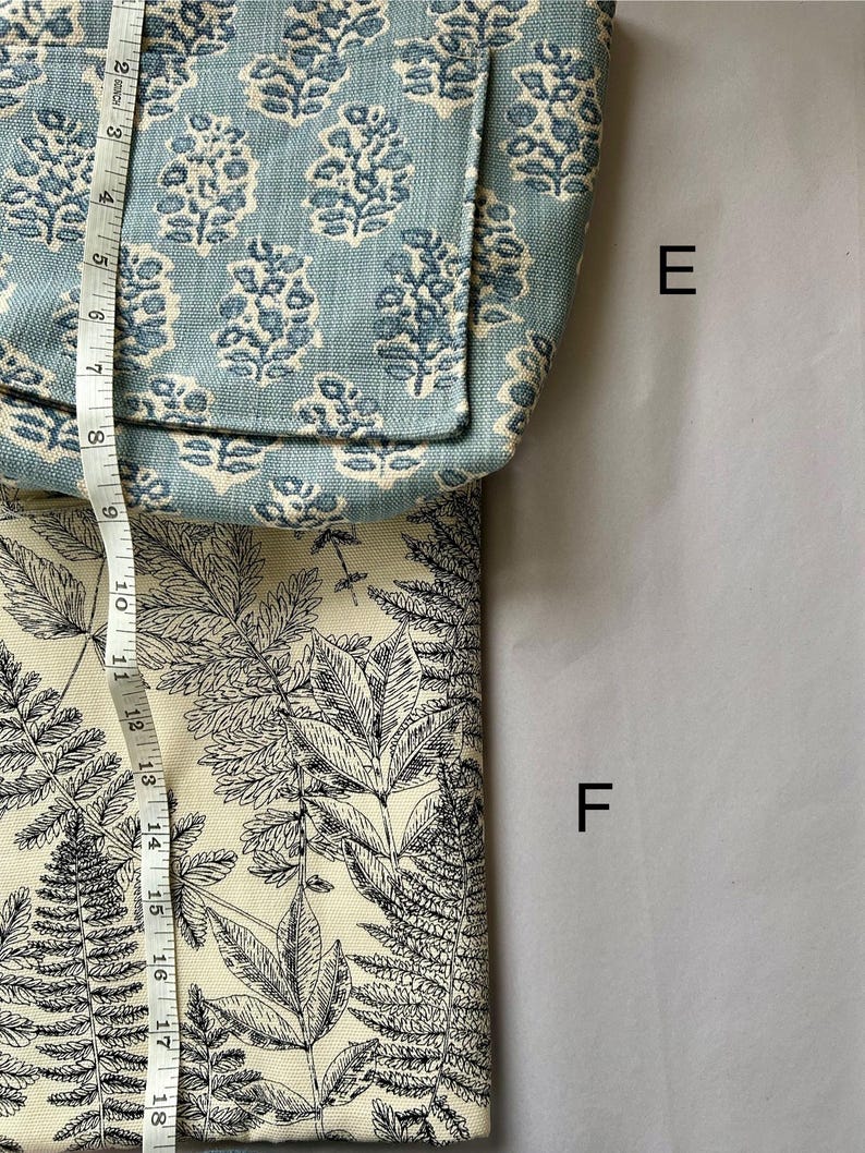 May include: A light blue tote bag with a floral pattern and a cream-colored fabric with a black fern design. The bag is approximately 8 inches wide. The cream fabric is approximately 10 inches wide.