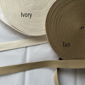 May include: Two spools of woven webbing in ivory and tan colors. The ivory spool has the word "Ivory" printed on it, and the tan spool has the word "Tan" printed on it. Two lengths of webbing are also visible.