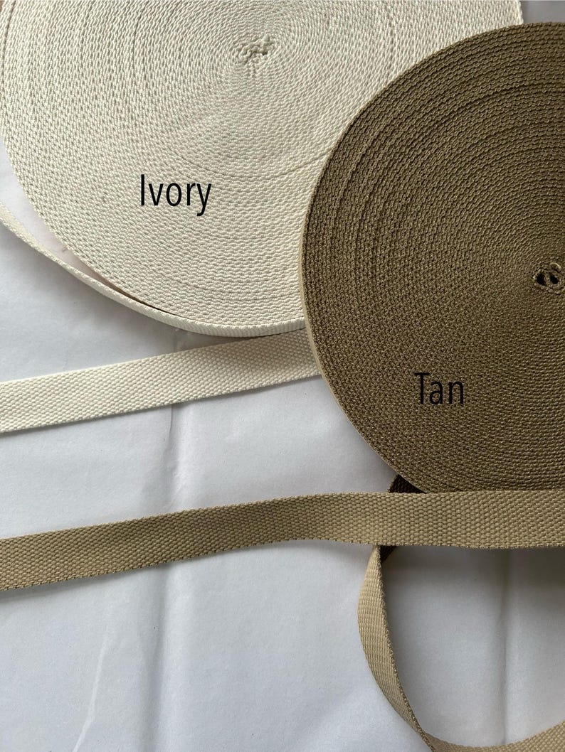 May include: Two spools of woven webbing in ivory and tan colors. The ivory spool has the word "Ivory" printed on it, and the tan spool has the word "Tan" printed on it. Two lengths of webbing are also visible.