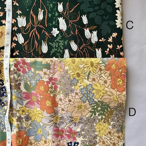 May include: Two fabric swatches with floral patterns. One is dark green with white tulip-like flowers and orange stems. The other is a mix of colorful flowers in shades of yellow, orange, pink, and blue. A measuring tape is visible.