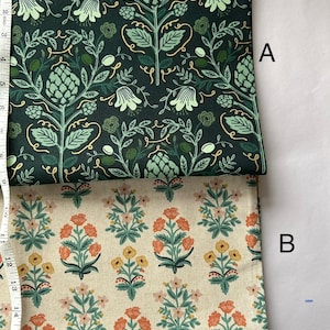 May include: Two fabric samples, labeled A and B, with floral patterns. Fabric A features a dark green background with light green and gold botanical designs. Fabric B has a cream background with orange, yellow, and green floral motifs. A measuring tape is visible.