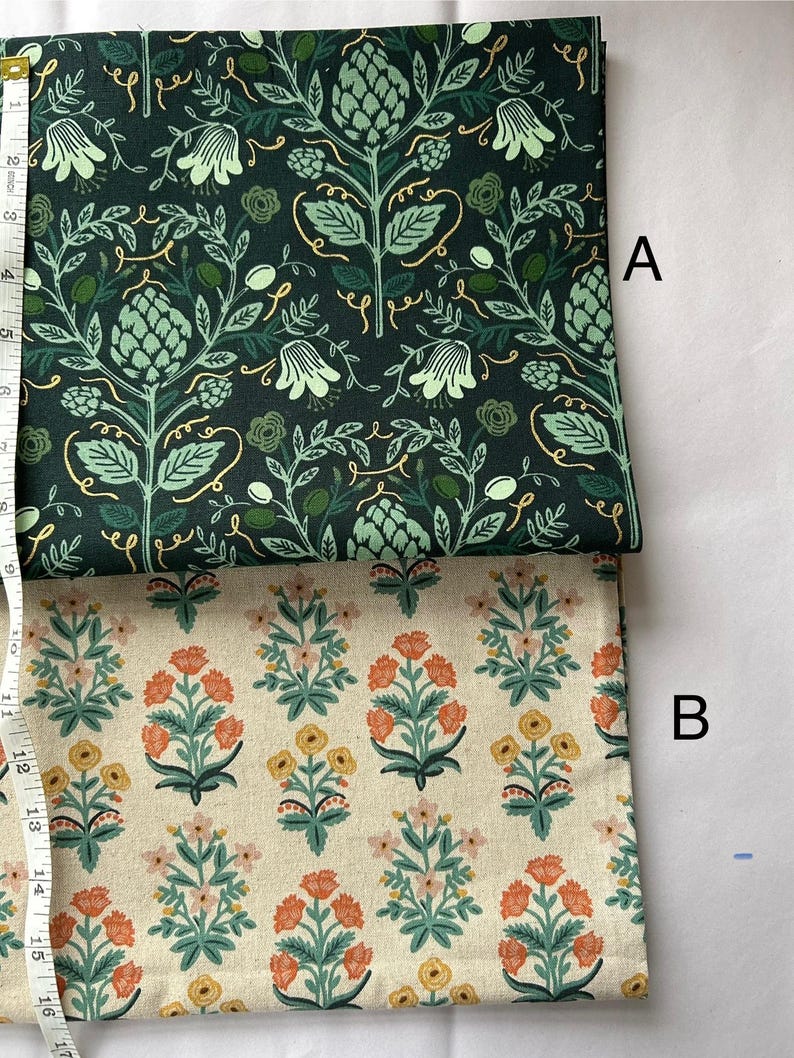May include: Two fabric samples, labeled A and B, with floral patterns. Fabric A features a dark green background with light green and gold botanical designs. Fabric B has a cream background with orange, yellow, and green floral motifs. A measuring tape is visible.