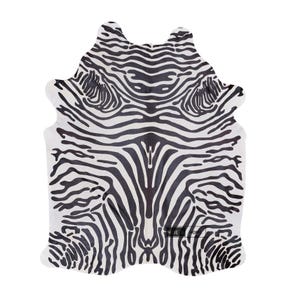 Puede incluir: Una alfombra con estampado de cebra en blanco y negro. La alfombra tiene una forma irregular, con bordes redondeados y un patrón que imita las rayas de una cebra. La alfombra está diseñada para parecerse a una piel de animal.