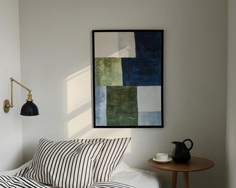 May include: A framed abstract art piece with a black border, featuring blocks of white, green, and navy blue. A black and white striped pillow and bedding are on a bed. A small, round wooden table holds a black pitcher and a white teacup.