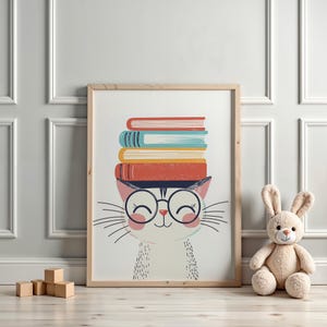 Könnte beinhalten: Gerahmter Druck mit einer Cartoon-Katze, die eine Brille trägt und einen Stapel bunter Bücher auf dem Kopf balanciert. Die Katze hat eine rosa Nase und Wangen mit langen Schnurrhaaren. Der Druck ist in einem hellen Holzrahmen.