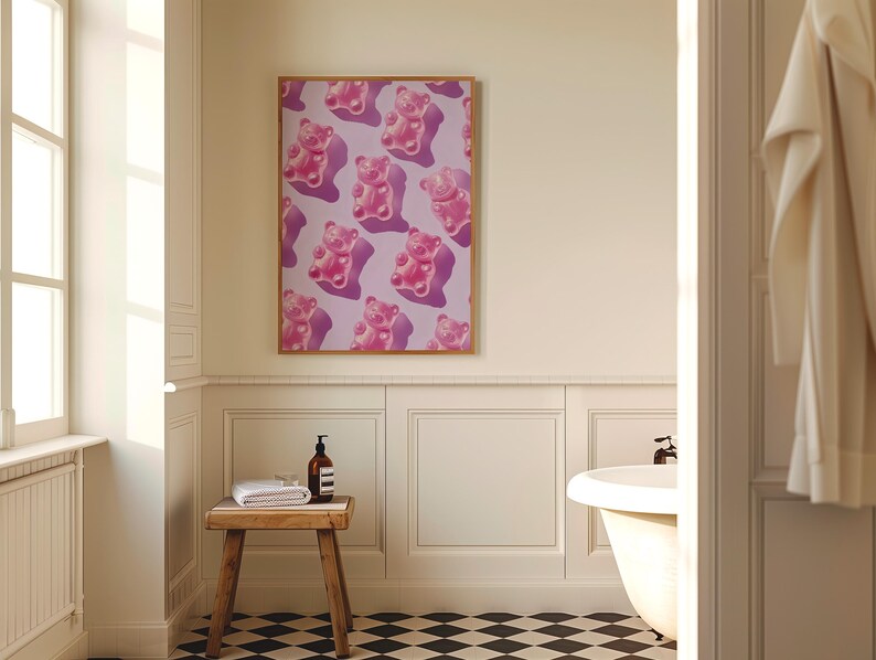 Pode incluir: Uma impress&atilde;o emoldurada com um padr&atilde;o repetitivo de ursinhos de goma rosa sobre um fundo lil&aacute;s claro. A obra de arte &eacute; exibida em um banheiro, adicionando um toque de cor &agrave; decora&ccedil;&atilde;o neutra.