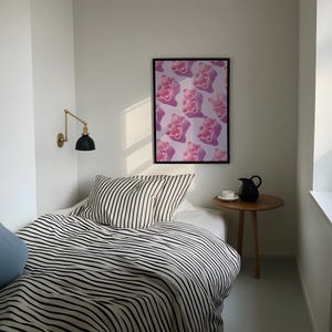 Pode incluir: Um quarto com uma cama com roupa de cama listrada em preto e branco e uma almofada azul clara. Uma impress&atilde;o emoldurada de ursinhos de goma rosa est&aacute; pendurada na parede. Uma pequena mesa lateral de madeira com um jarro preto e uma x&iacute;cara branca.