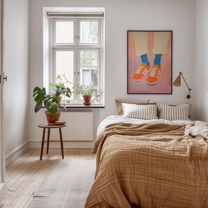 May include: A bedroom with a bed with a brown blanket and white and gray striped pillows. There is a painting above the bed of a pair of orange shoes with blue socks. There is a plant in a pot on the windowsill and a small wooden stool next to the plant.