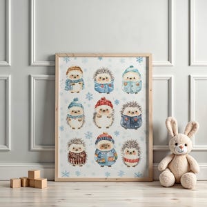 May include: A framed print featuring nine watercolor hedgehogs, each wearing winter clothing like hats, scarves, and coats. The background is light blue with snowflake illustrations. The frame is made of light-colored wood.