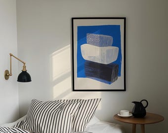 May include: A framed abstract print with a blue background and white and black geometric shapes. The print is hanging on a white wall above a striped bedspread.