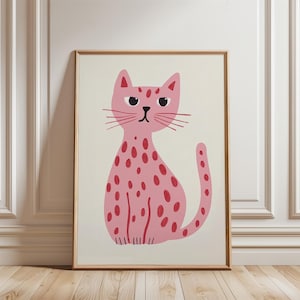 Può includere: Stampa incorniciata con un gatto rosa con macchie rosse. Il gatto ha occhi neri e baffi. L'opera d'arte è ambientata su uno sfondo color crema e incorniciata in una cornice di legno marrone chiaro. Il gatto è seduto.
