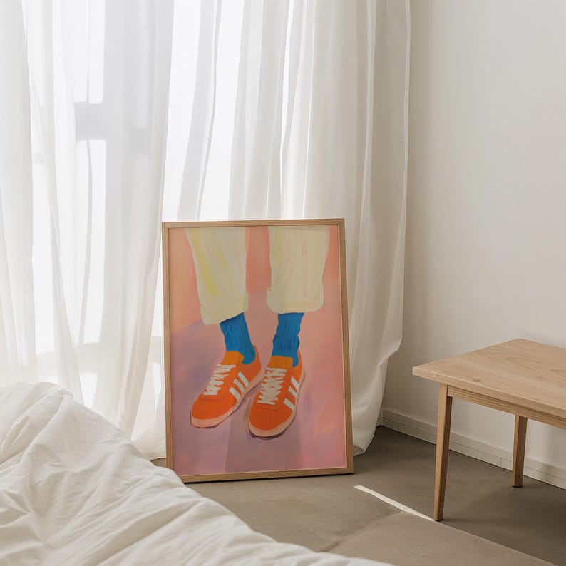 May include: A framed painting of a pair of legs wearing orange sneakers with white stripes and blue socks. The background is a soft pink with a light purple gradient.