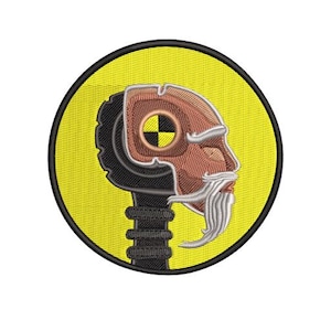 Puede incluir: Parche bordado amarillo con una cabeza negra y marrón con un símbolo de diana amarillo y negro en el lateral. La cabeza tiene una barba blanca y lleva un casco negro.