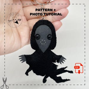May include: A handmade black felt keychain in the shape of a hooded figure with button eyes. The keychain has a silver ring and the text "PATTERN + PHOTO TUTORIAL". The PDF icon is visible.
