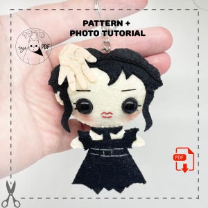 May include: A black and white felt doll with black hair and a black dress. The doll has large eyes and a red mouth. The doll is being held by a hand. The image includes the text "PATTERN + PHOTO TUTORIAL".