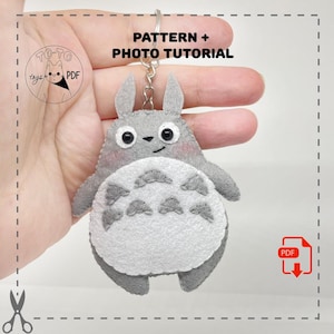 May include: A gray felt Totoro keychain with a white belly and black eyes. The keychain has a silver ring and the text "PATTERN + PHOTO TUTORIAL". The product is a PDF pattern.