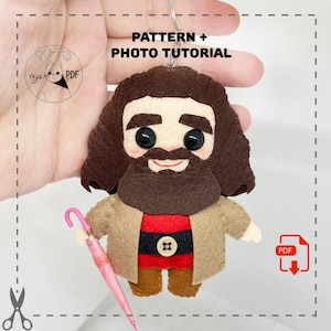 May include: A handmade felt keychain featuring a character with a brown beard, hair, and a tan coat. The character is holding a pink umbrella. The keychain has the text "PATTERN + PHOTO TUTORIAL".