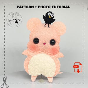 Op de afbeelding: Een roze viltmuis met een zwarte viltvogel op zijn kop. De muis heeft zwarte ogen en een witte buik. Het patroon en de fototutorial zijn beschikbaar als PDF-download. De tekst "PATTERN + PHOTO TUTORIAL" staat bovenaan de afbeelding. De tekst "TOTO toys PDF" staat in een cirkel linksboven in de afbeelding. Een PDF-pictogram staat rechtsonder in de afbeelding.