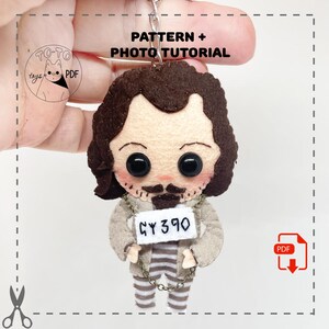 May include: A handmade felt doll keychain featuring a cartoon character with dark hair, a mustache, and a prisoner tag that reads "GY390." The doll is wearing a striped shirt and pants. The image includes the text "PATTERN + PHOTO TUTORIAL."