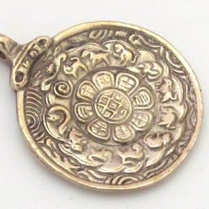 May include: A gold-colored, circular pendant with intricate relief carvings. The pendant features a central floral design surrounded by animal and abstract motifs. It has a small loop for hanging and is likely a piece of jewelry or decorative item.