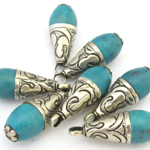 May include: A collection of turquoise-colored, teardrop-shaped beads with ornate silver-colored metal caps. Each bead has a small loop for stringing. The beads are scattered against a white background, showcasing their unique design and color.