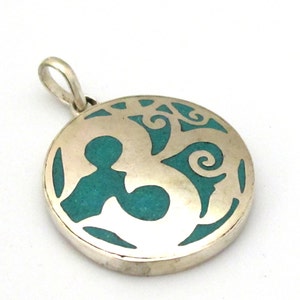 May include: A silver pendant with a circular design. The pendant features a turquoise inlay and a cut-out pattern. The design includes abstract shapes and swirls. The pendant has a loop for a chain.