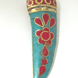 May include: A turquoise pendant with a brass bail and gold trim. The pendant features a red floral design and a red decorative border. The pendant is approximately 3 inches long.