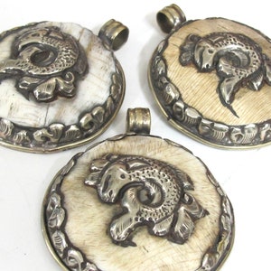 May include: Three oval pendants with a silver ram design on a cream-colored background. The ram is detailed with curved horns and floral accents. Each pendant has a silver border and a small loop at the top for a chain.