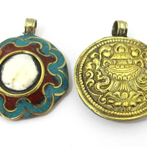 May include: Two ornate pendants. One features a turquoise and red enamel design with a central white stone. The other is a gold-colored pendant with an embossed floral and vessel design. Both have gold-colored loops for hanging.