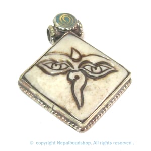 May include: Cream-colored, diamond-shaped pendant with a silver-colored border. The pendant features a detailed, dark brown illustration of two eyes and a teardrop shape. A small, round, turquoise-colored accent is at the top.