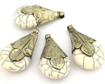 May include: Four teardrop-shaped pendants with a cream-colored, cracked stone design and antique silver-colored metal caps. The caps feature a leaf design and a loop for stringing. These pendants are suitable for jewelry making.