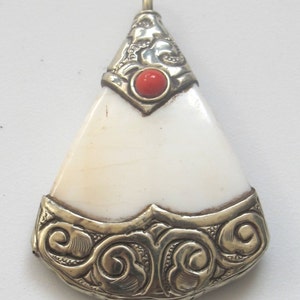 May include: A pendant with a triangular, off-white central piece. The pendant is framed with ornate silver-colored metalwork. A small, round, red stone is set near the top. The pendant has a loop for a chain.