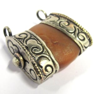 May include: A pendant with a rectangular, amber-colored center stone. The stone is encased in ornate silver metal with decorative scrollwork and a small loop at each end for a chain. The edges are accented with gold.