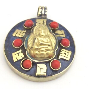 May include: A gold-colored pendant with a seated Buddha figure in the center. The pendant has a dark blue enamel background with red coral-like beads and gold-colored accents. The pendant is round with a loop at the top for a chain.
