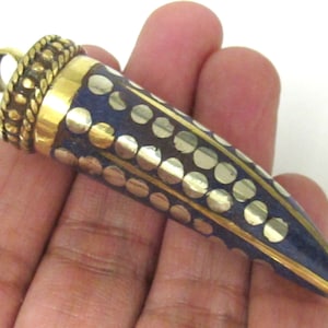 May include: A pendant with a brass loop and a conical shape. The pendant features a dark blue surface with a pattern of gold-colored circles and lines. The top of the pendant has a textured brass design.